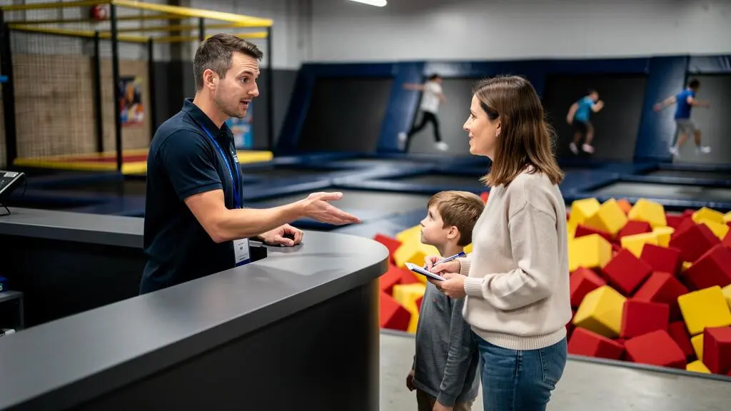 Un membre du personnel d'un parc de trampolines présente une formule d'anniversaire à une mère et son enfant à l'accueil.
